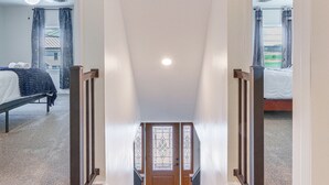 Ein Flur, der in ein Schlafzimmer mit Bett, einem Vorhangfenster und einem Deckenventilator führt.