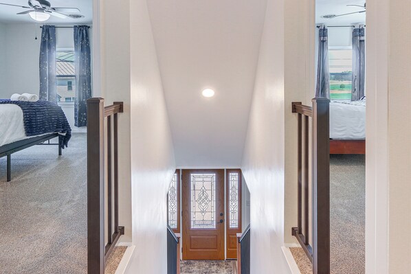 A hallway leading to a bedroom with a bed, a window with curtains, and a ceiling fan.