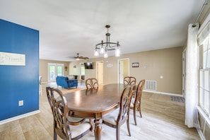 A dining room with a large wooden table surrounded by chairs, a chandelier, and a blue accent wall. - Milledgeville Home w/ Game Room & Private Dock! (Milledgeville)