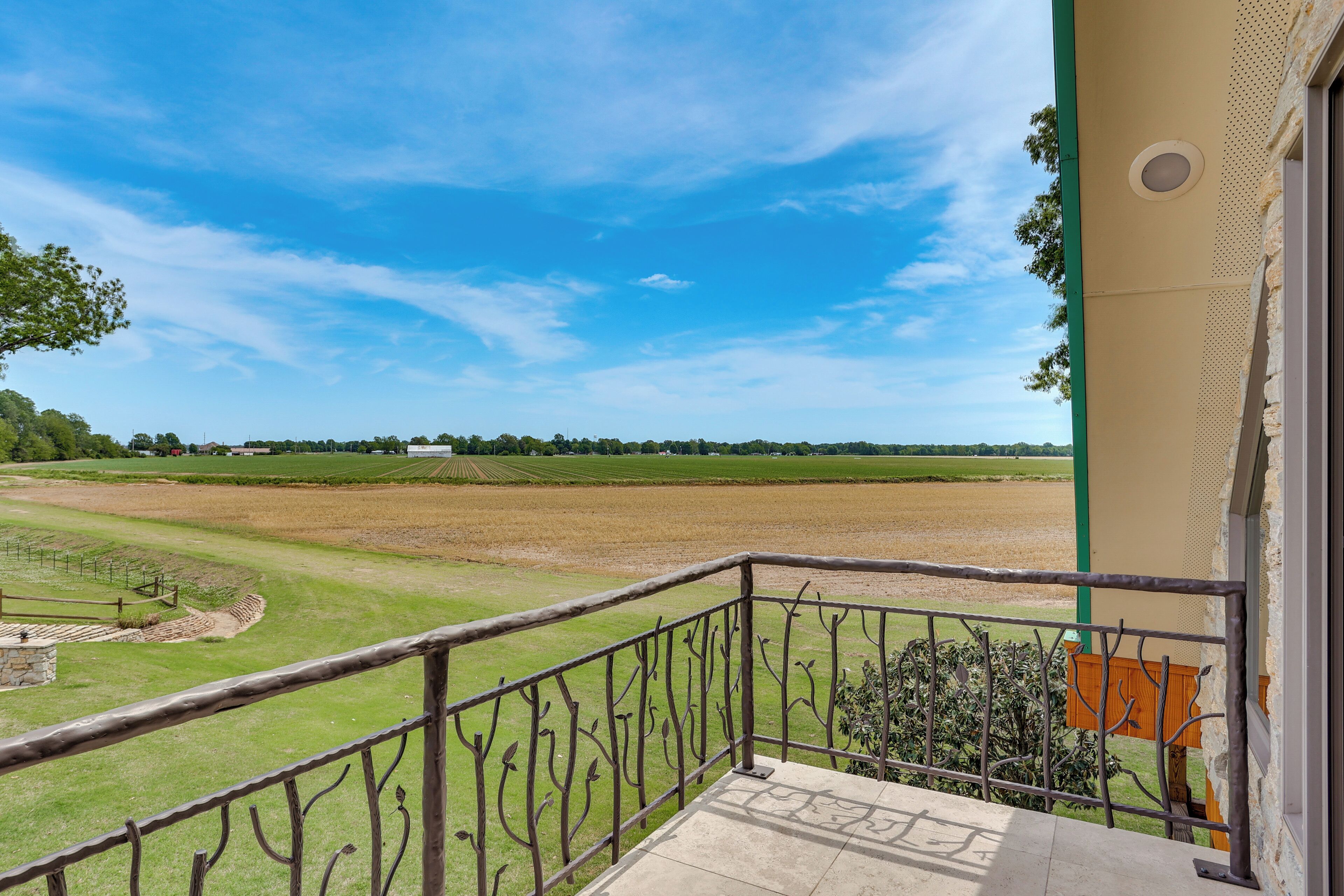 A balcony with a view of a large, open field and distant trees under a clear sky.