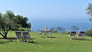 A grassy outdoor area with three lounge chairs and a table with a vase of flowers. - Modern Villa with Pool and Breathtaking Views on the Enchanting Amalfi Coast! (Amalfi)