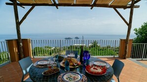 A table set for a meal on a terrace with a view of the sea and distant islands. - Charming Villa with Pool, Overlooking the Enchanting Galli Islands (Amalfi)
