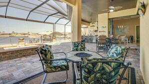 A covered outdoor seating area with chairs and tables, overlooking a pool and poolside area.