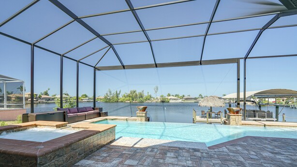 An outdoor swimming pool with a hot tub, seating area, and a view of a lake.