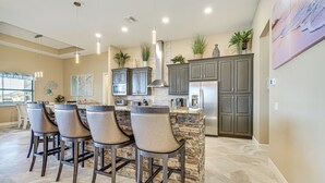 A modern kitchen with a central island, bar stools, granite countertops, and built-in appliances.