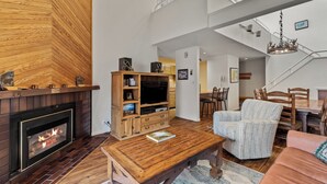 Amplia sala de estar con chimenea, mueble de entretenimiento de madera y un comedor con escalera.