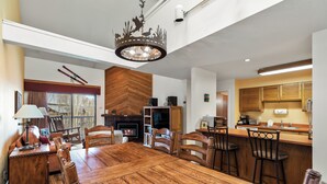 Un comedor amplio con una gran mesa de madera y sillas, chimenea y una zona de cocina con armarios de madera y barra.