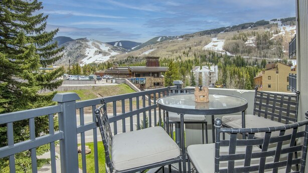 A balcony with a round table and chairs, overlooking a mountainous landscape with buildings and trees. - Vantage Point #307 2 Bedroom Condo by RedAwning (Vail)