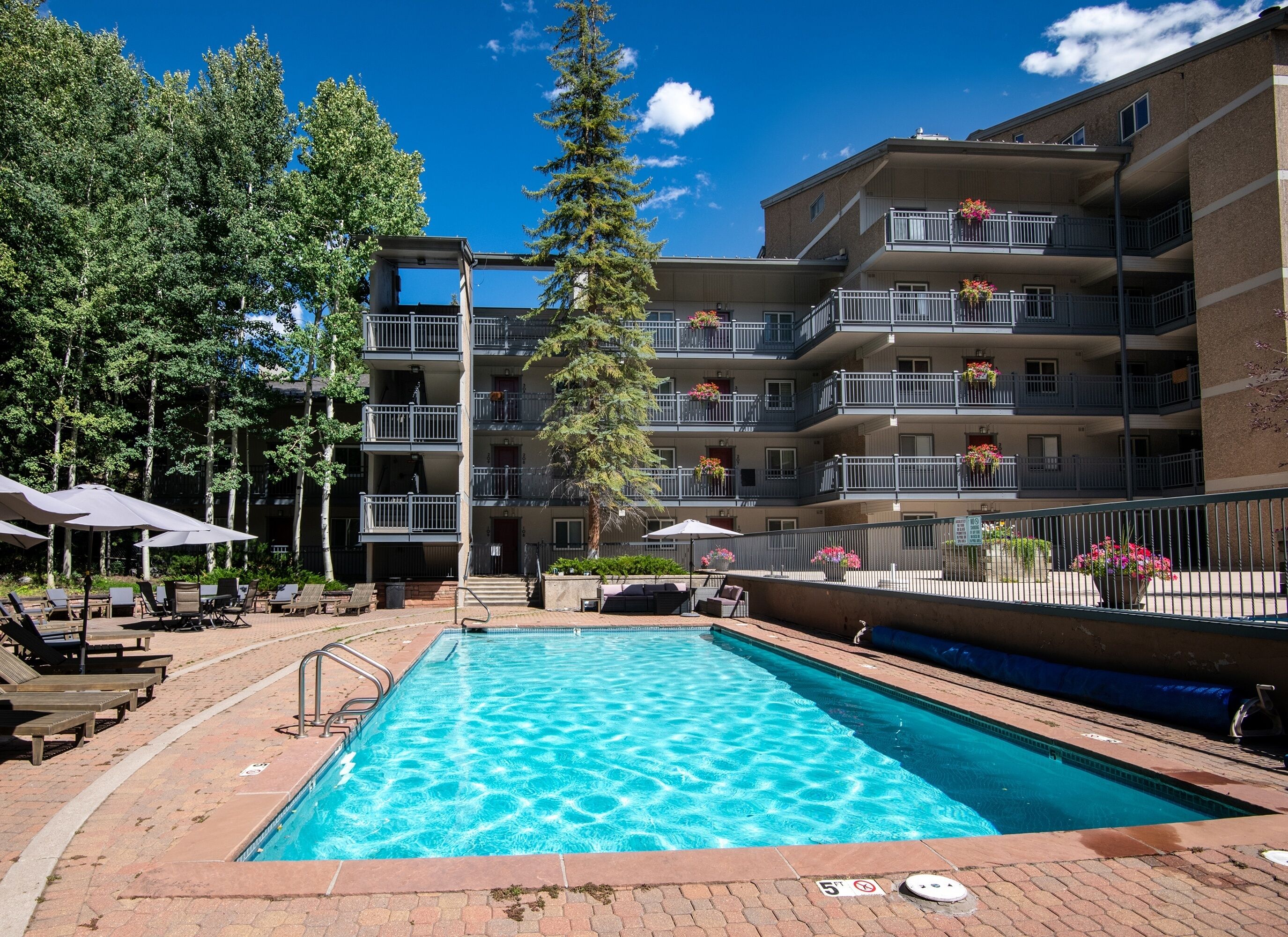 A swimming pool with lounge chairs and umbrellas, surrounded by multi-story buildings with balconies.