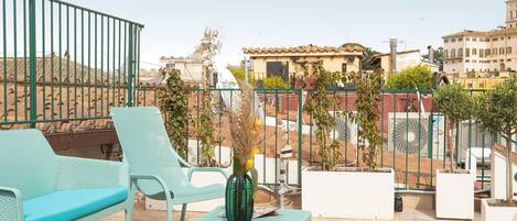 A rooftop terrace with turquoise chairs and a table, surrounded by a metal railing.