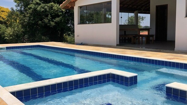 Una piscina rectangular con azulejos azules, rodeada por una terraza de madera y un edificio blanco con grandes ventanales.