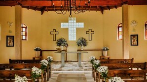 Interior de iglesia con bancos de madera, un altar central y dos grandes cruces en las paredes.