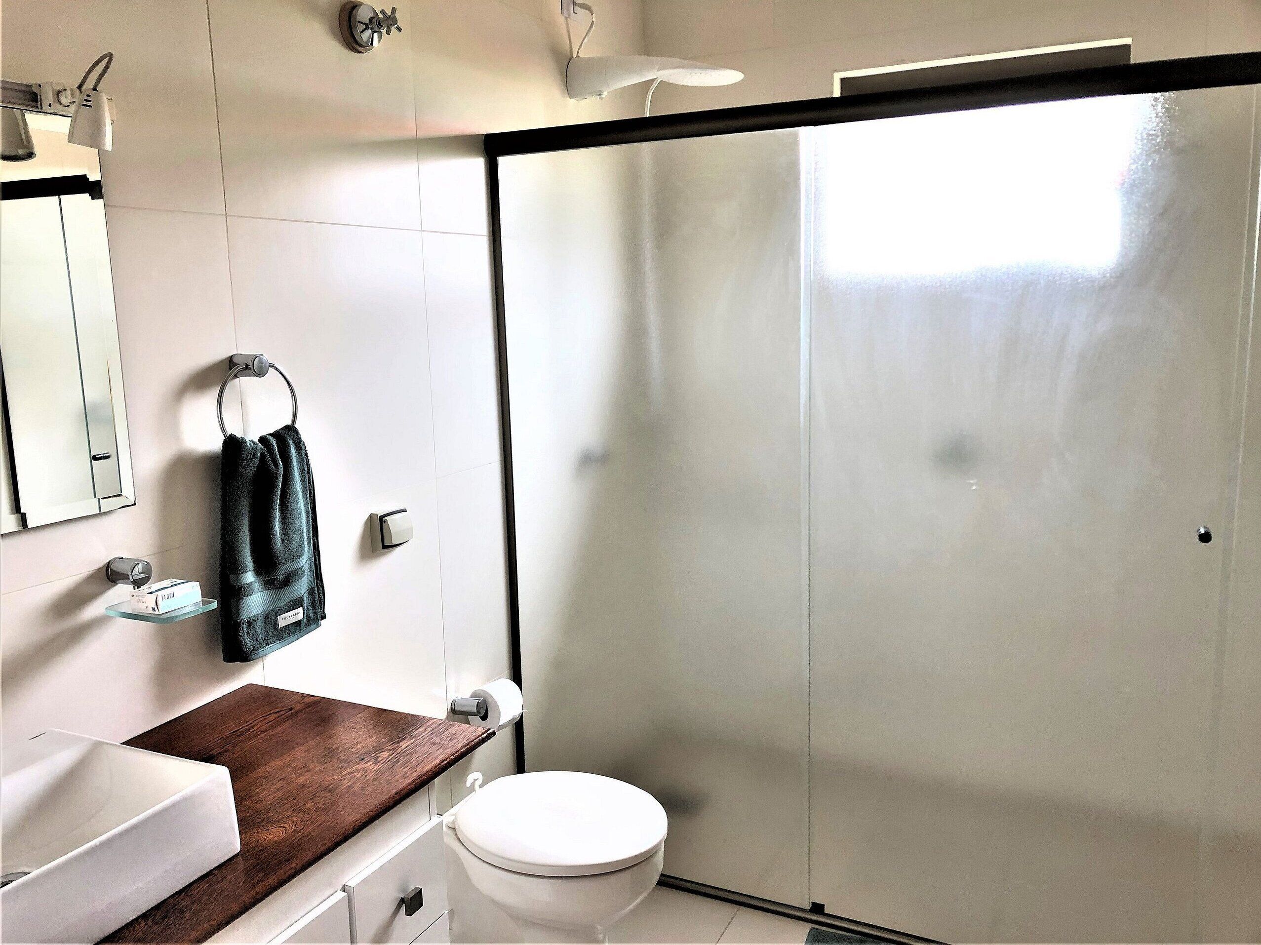 A bathroom with a white toilet, a wooden vanity, a towel rack, a mirror, and a frosted glass shower door.