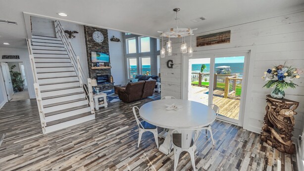 A spacious living area with a wooden staircase, a round dining table, and a view of the ocean through large windows.