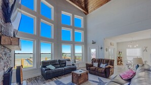 A spacious living room with large windows, a stone wall, and a view of the ocean.