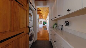 Une buanderie avec des armoires en bois, un lave-linge et un couloir menant à une chambre décorée avec un motif équestre vert.
