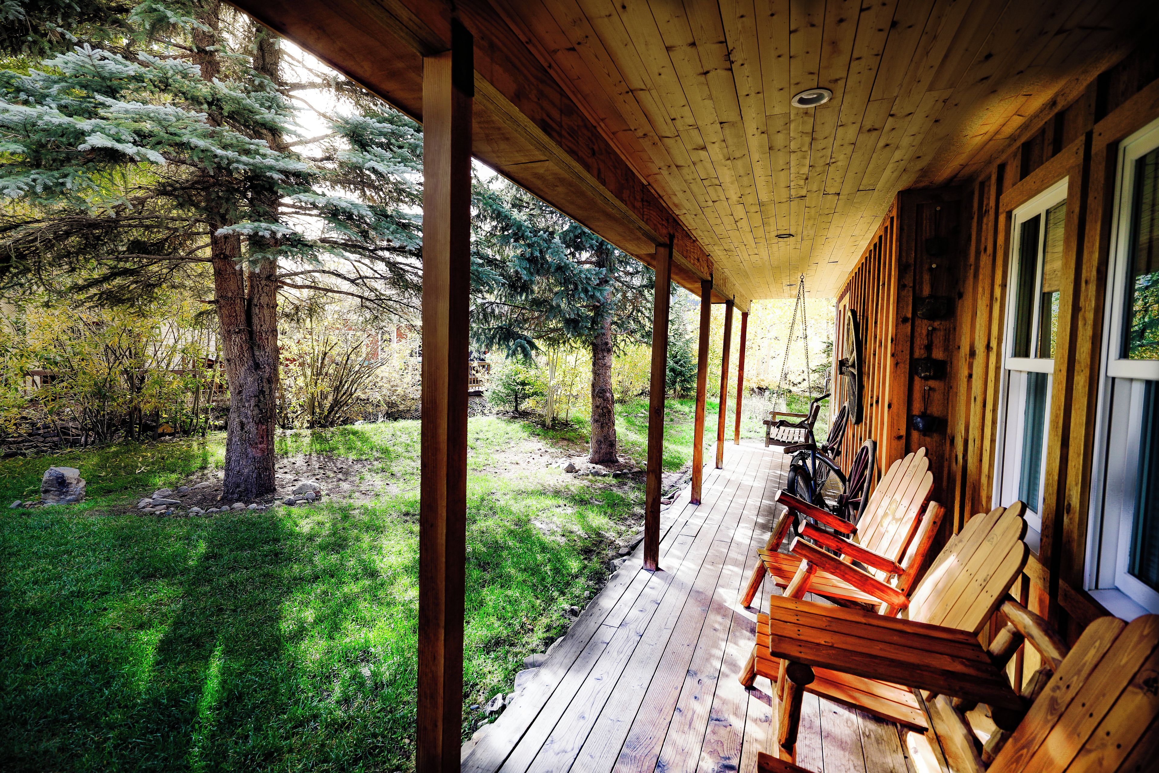A wooden porch with chairs, a bicycle, and a view of a forested area.
