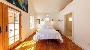 Une chambre avec un grand lit, un plancher en bois et un tableau accroché au mur.