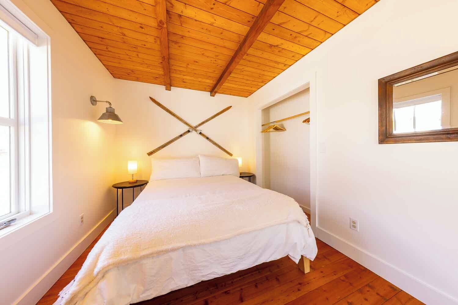 Une chambre avec un plafond en bois, un lit avec une literie blanche, une table de chevet avec une lampe et un miroir sur le mur.