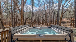 A hot tub in a wooded area with a stone exterior and metal railing.