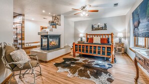 A cozy living room with a fireplace, a large bed, and a ceiling fan.