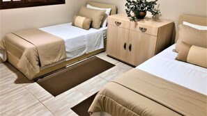 A hotel room with two beds, a wooden wardrobe, a small potted plant, and a brown rug.