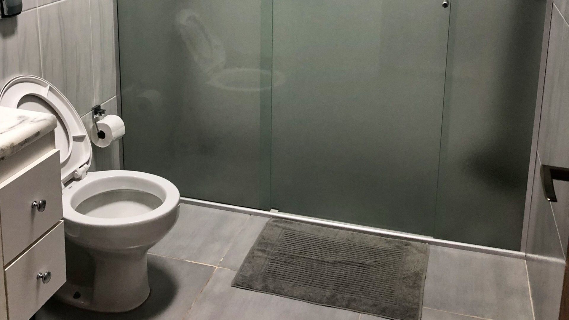 Une salle de bain moderne équipée de toilettes, d’une douche et d’un plan de toilette en marbre.