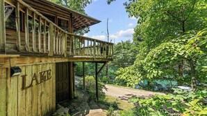 A wooden cabin with a balcony, surrounded by lush greenery and a clear sky. - Historic Cabin, Peaceful, Waterside, Patio Firepit (Eureka Springs)