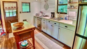 A kitchen with wooden cabinets, a built-in oven, a sink, and a window with a view of greenery. - Historic Cabin, Peaceful, Waterside, Patio Firepit (Eureka Springs)