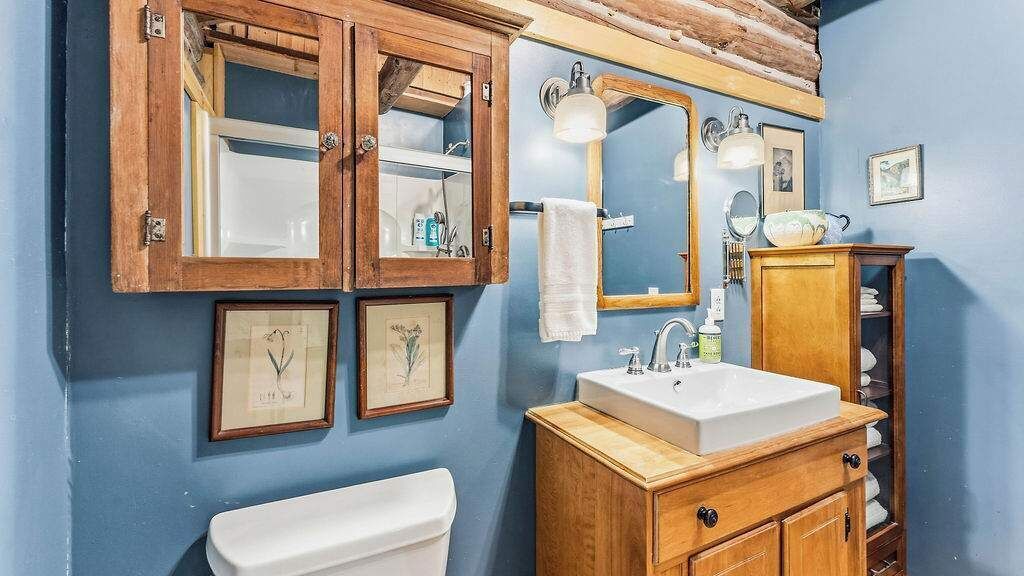 A bathroom with wooden cabinets, a white sink, a mirror, and framed pictures on the wall.