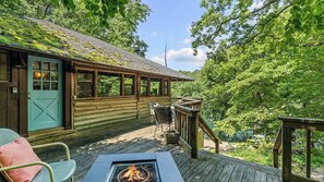 A wooden cabin with a deck, a fire pit, and a view of the surrounding forest. - Historic Cabin, Peaceful, Waterside, Patio Firepit (Eureka Springs)