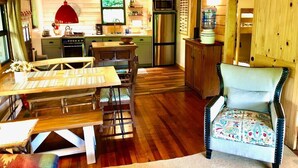 A rustic kitchen with wooden cabinets, a dining table, and a chair. - Historic Cabin, Peaceful, Waterside, Patio Firepit (Eureka Springs)
