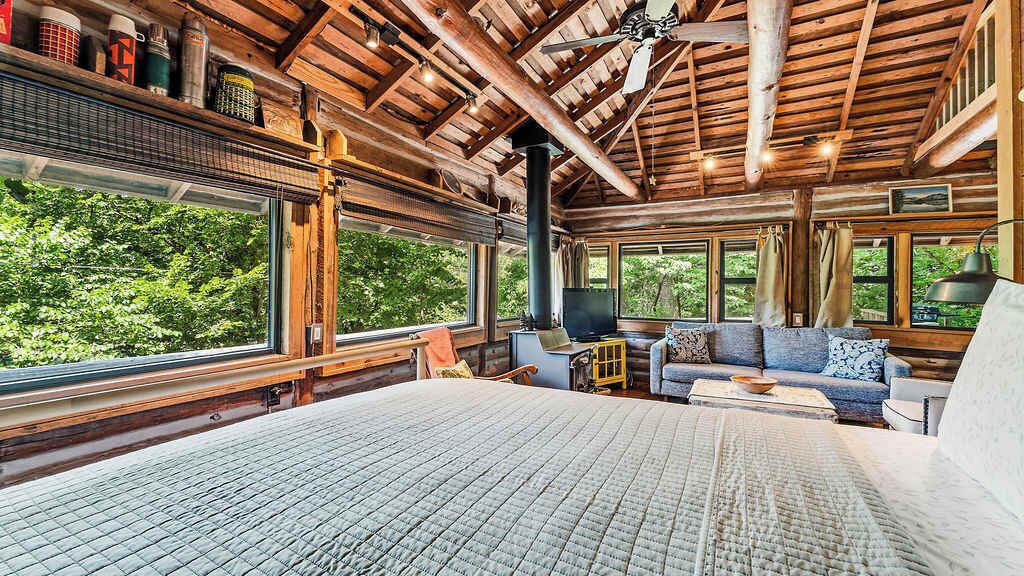 A log cabin interior with a large bed, a sofa, and a fireplace.