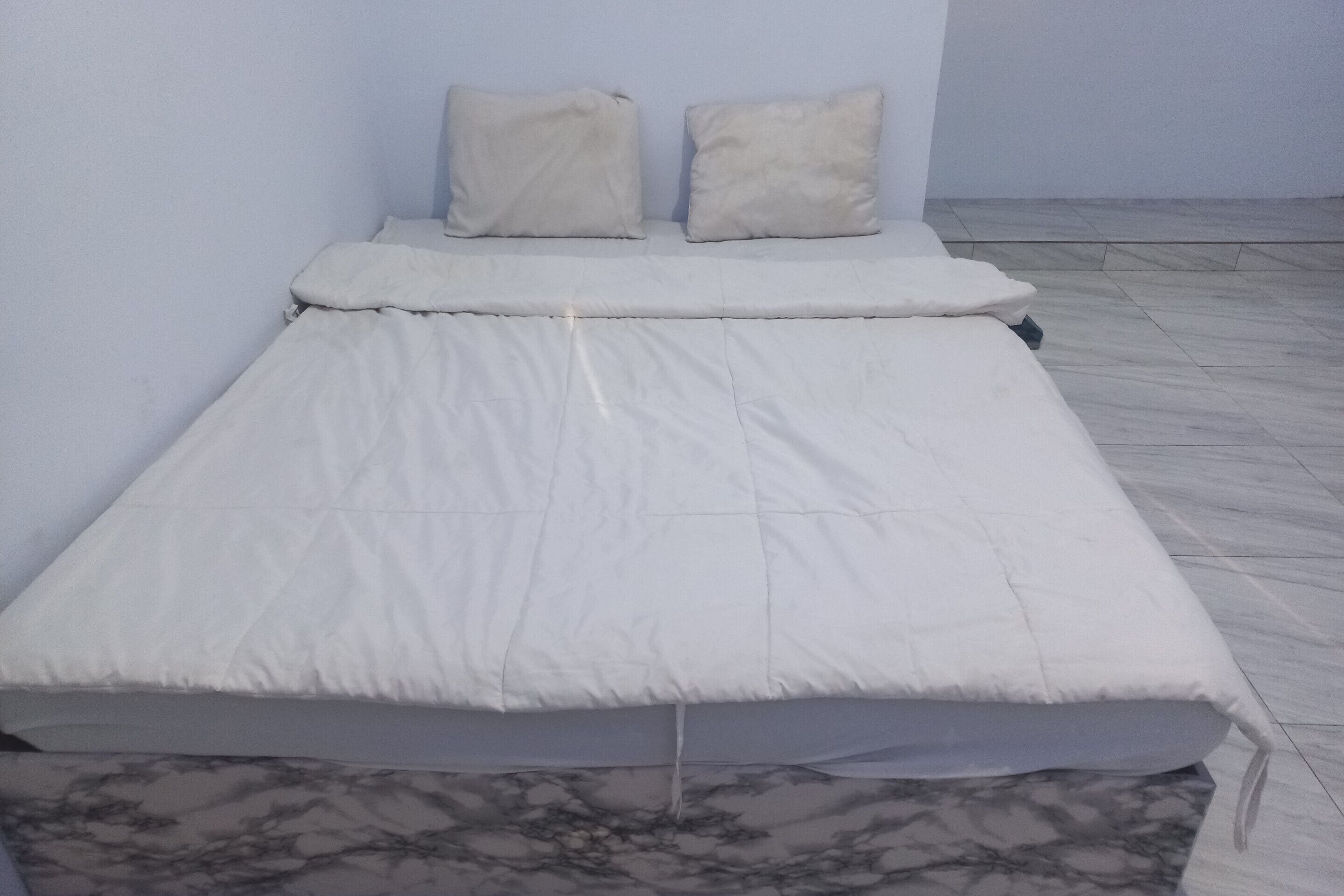 A single bed with white bedding in a room with a tiled floor and plain walls.
