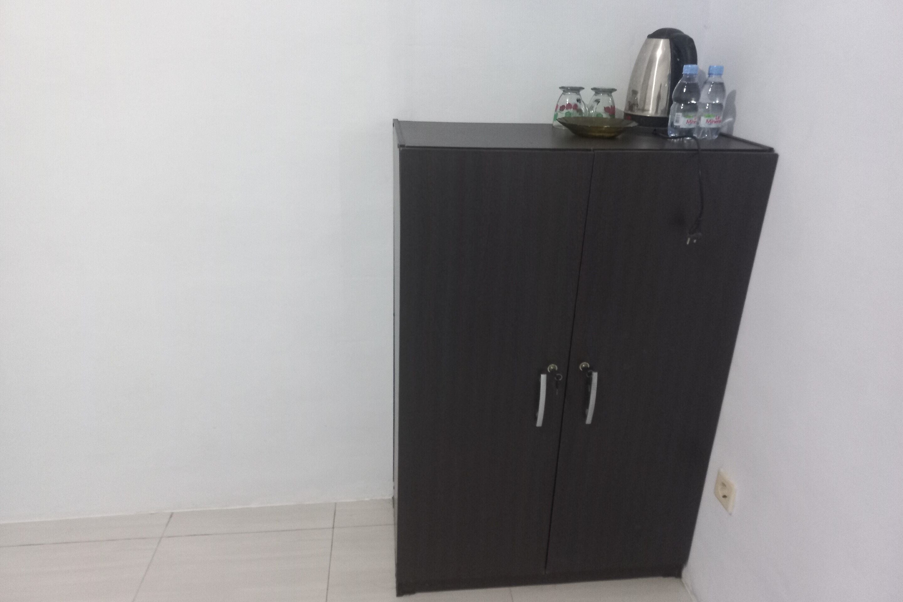Un armario oscuro con dos puertas y tiradores, una tetera y dos botellas de agua encima.