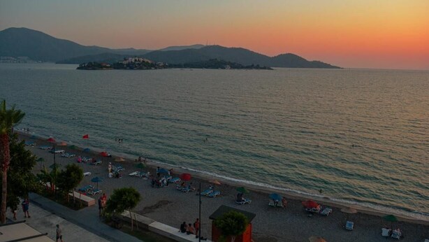 A beach with umbrellas and lounge chairs, a calm sea, and distant hills. - Er-Öz Hotel & Restaurant (Fethiye)