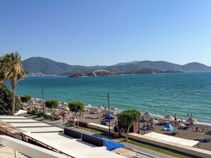 A beach with umbrellas, lounge chairs, and a view of the sea and hills. - Er-Öz Hotel & Restaurant (Fethiye)
