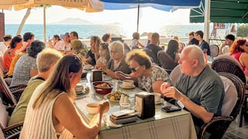 A group of people dining at an outdoor restaurant with a view of the sea.