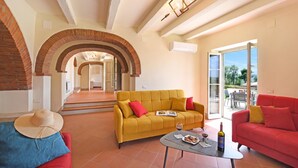A spacious living area with a yellow sofa, red sofa, and a coffee table. There is a brick archway leading to another room, and a glass door to an outdoor area. - Amazing Villa Chimera Green 10 Pool&Gym  (Arezzo)