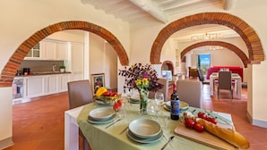 A dining area with a table set for four, a vase with flowers, and a kitchen in the background. - Amazing Villa Chimera Green 10 Pool&Gym  (Arezzo)