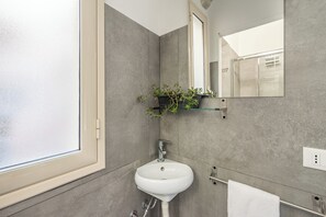 Un bagno con un lavandino bianco, uno specchio e una finestra.