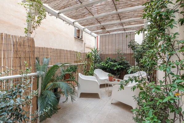 Un'area patio coperta con sedie di plastica bianca, un tavolino e diverse piante in vaso.