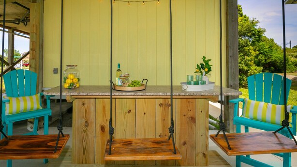 Un ensemble de balançoires en bois avec une table au centre, entouré de chaises turquoise dotées de coussins à rayures jaunes et blanches.