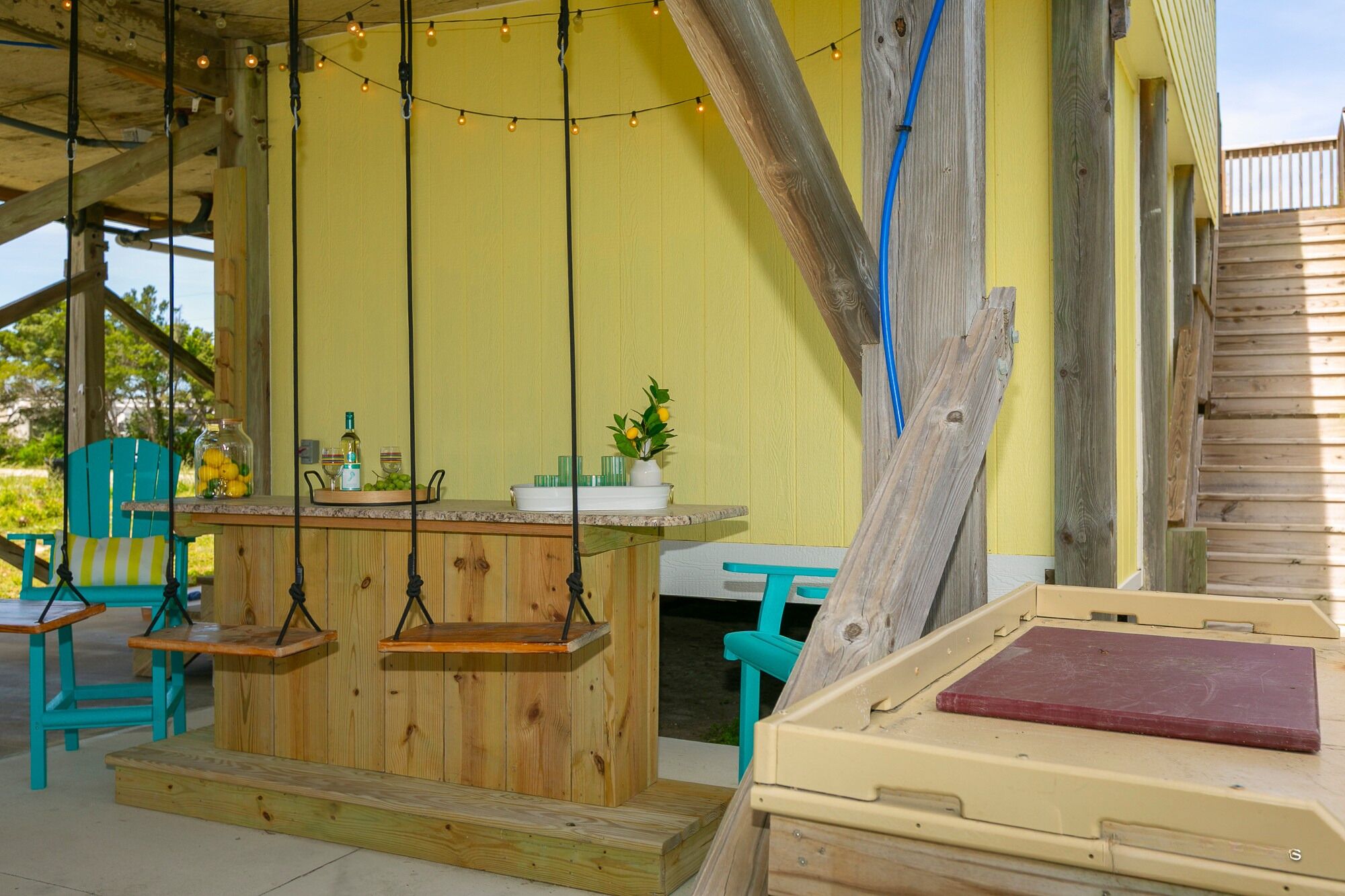Un coin bar en bois avec un luminaire suspendu, une petite table sur laquelle est posé un vase de citrons et une chaise bleue.