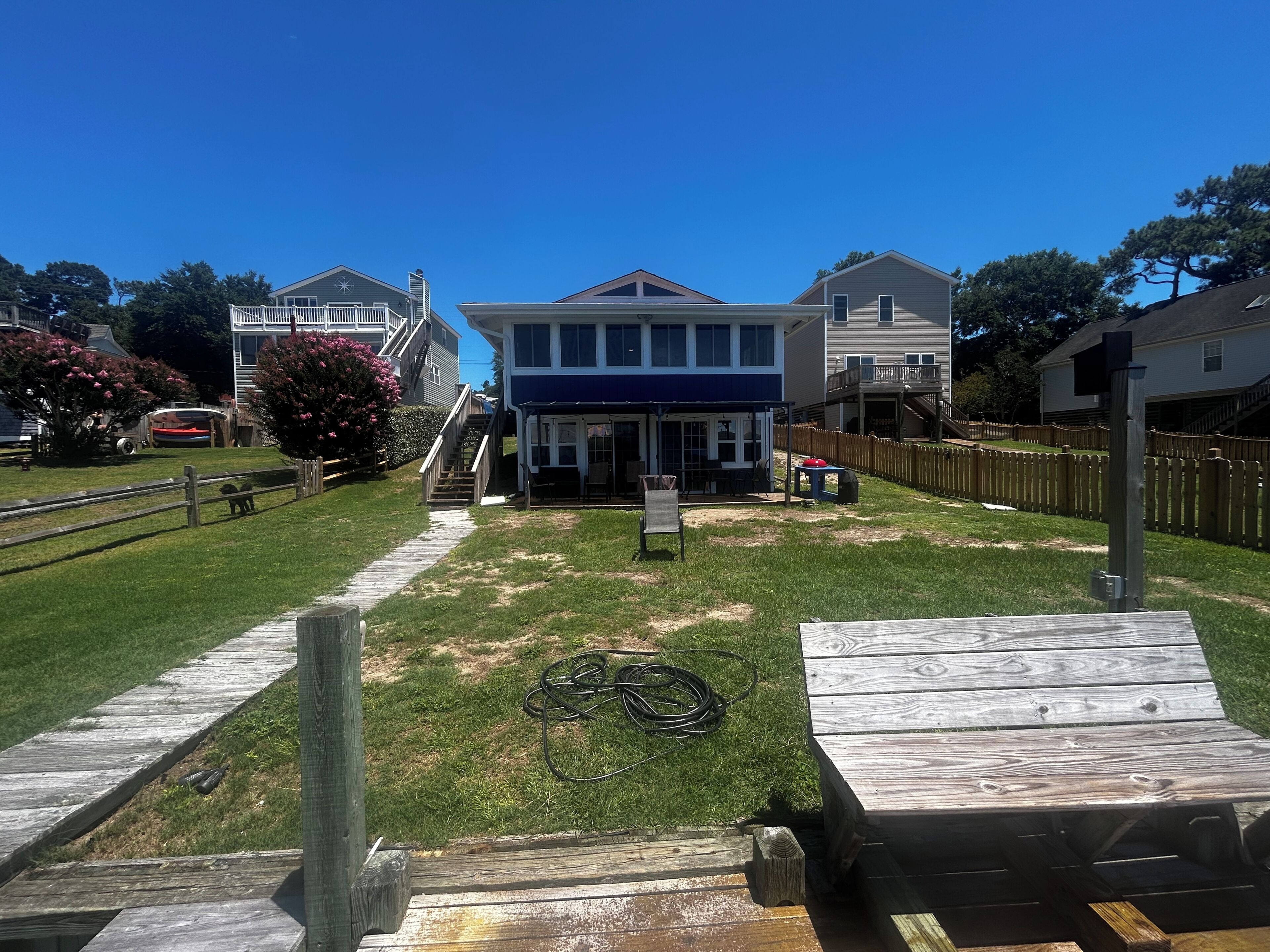 A residential area with a two-story house, a wooden deck, and a fenced yard.