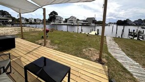 A wooden deck with a covered area, overlooking a body of water with docks and houses in the background. - SunsetSanctuary-CanalFront/DogFriendly/Pool&Tennis (Kill Devil Hills)
