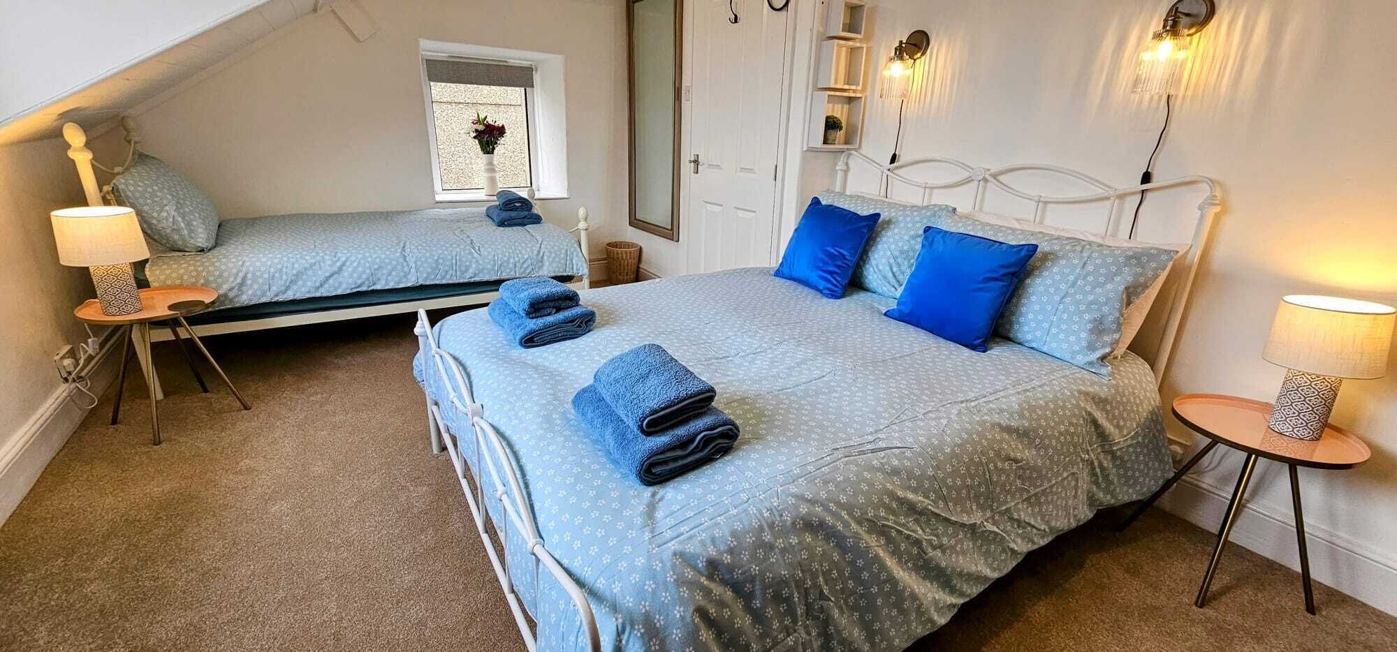 Une chambre à coucher avec deux lits, chacun recouvert d’une courtepointe et agrémenté d’oreillers aux motifs bleus, ainsi qu’une petite table avec une lampe.
