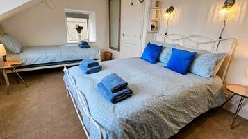 Une chambre à coucher avec deux lits, chacun recouvert d’une courtepointe et agrémenté d’oreillers aux motifs bleus, ainsi qu’une petite table avec une lampe.