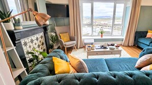 Un salón con un conjunto de sofás, una mesa de centro y vistas a un puerto deportivo a través de amplios ventanales.