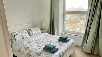 Een slaapkamer met een bed, een raam met gordijnen en uitzicht op een landschap.